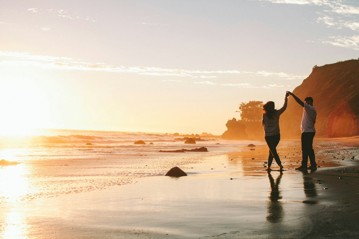 Two people walking on a beach at sunset